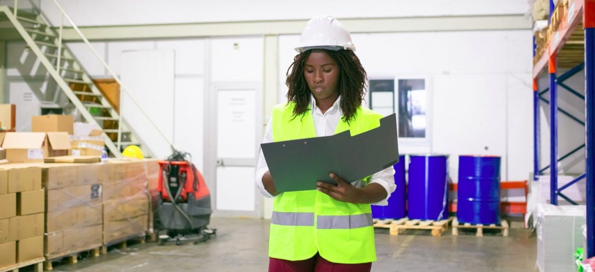 focused-female-logistic-employee-hardhat-safety-vest-walking-warehouse-carrying-open-folder-looking-through-document-copy-space-front-view-labor-inspection-concept-1536x1025